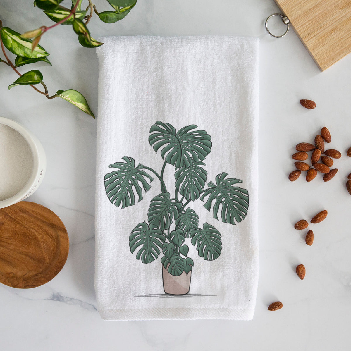White hand towel printed with a full-color illustration of a large potted Monstera plant.