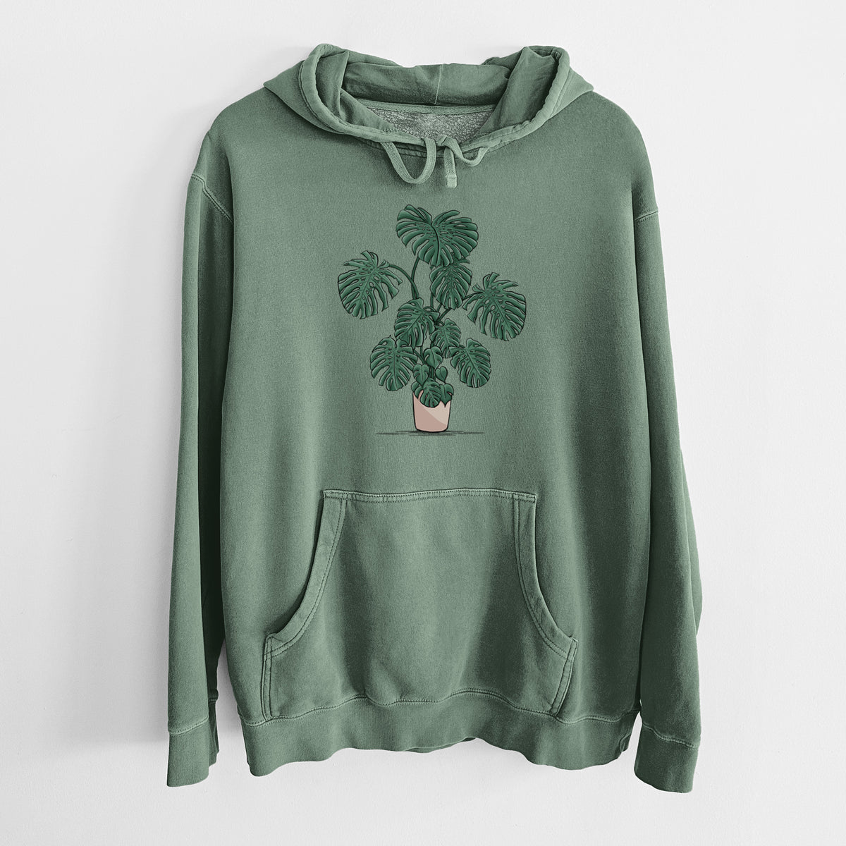 Alpine green pigment dyed hoodie laid flat, printed with a full-color illustration of a large potted Monstera plant.