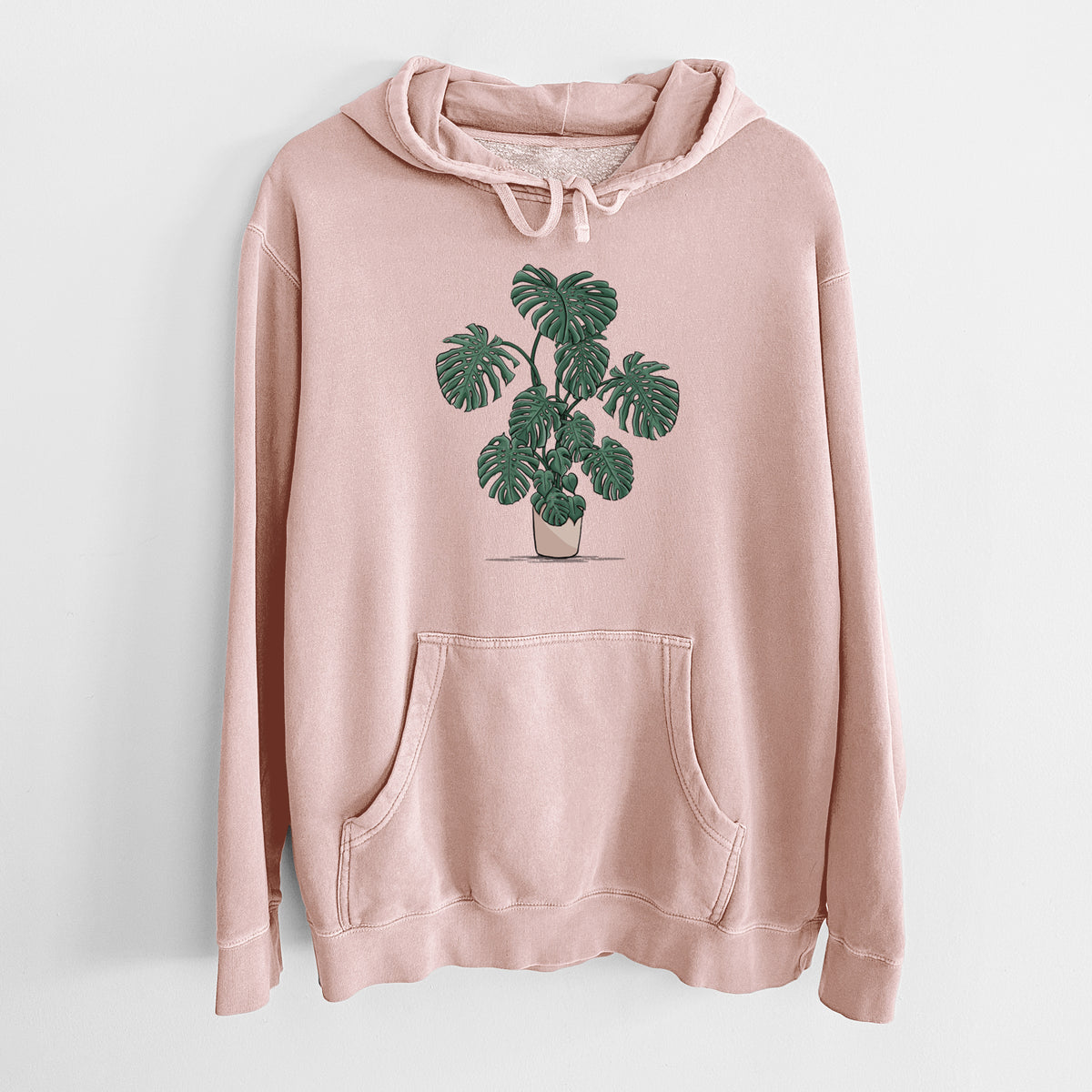Dusty pink pigment dyed hoodie laid flat, printed with a full-color illustration of a large potted Monstera plant.