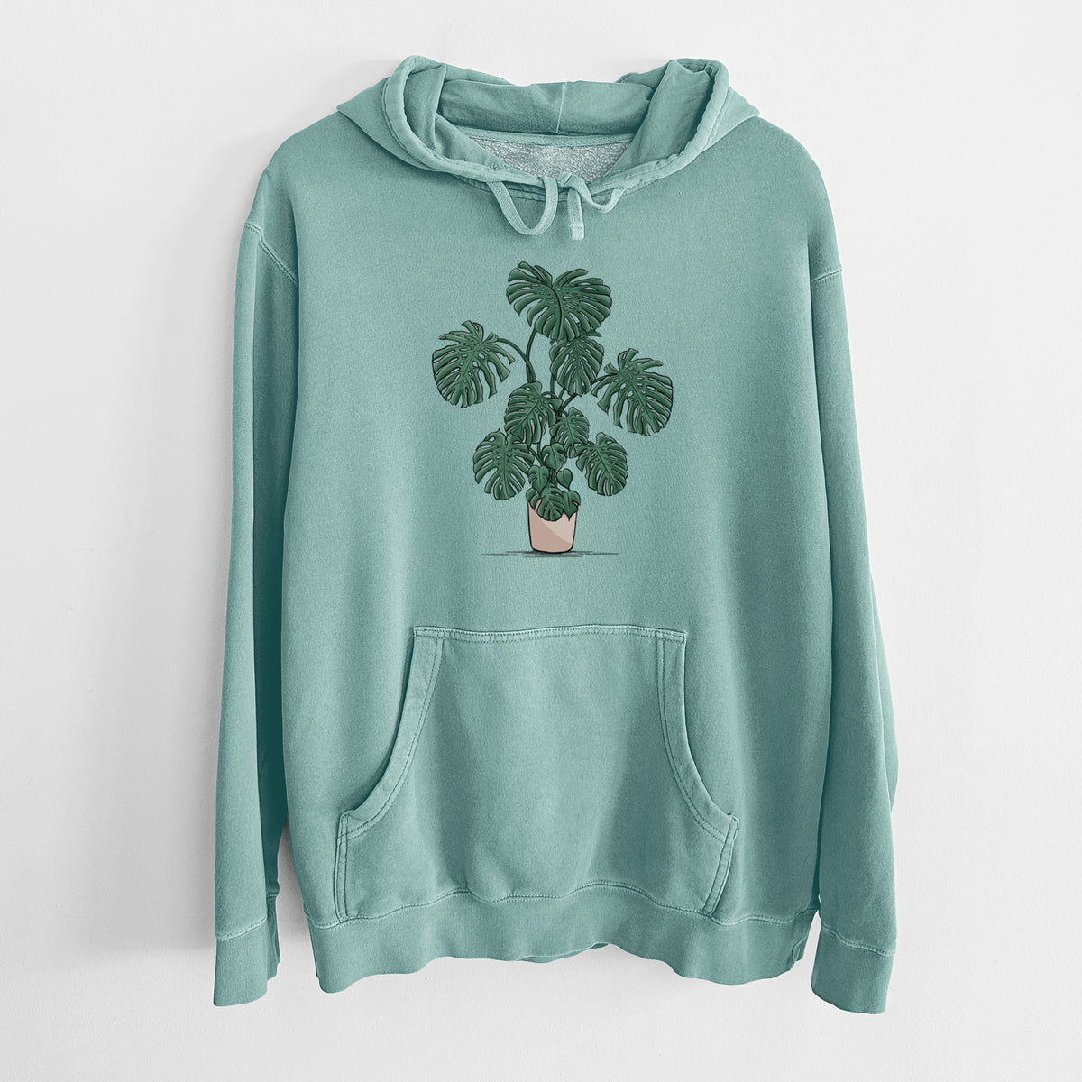 Mint green pigment dyed hoodie laid flat, printed with a full-color illustration of a large potted Monstera plant.