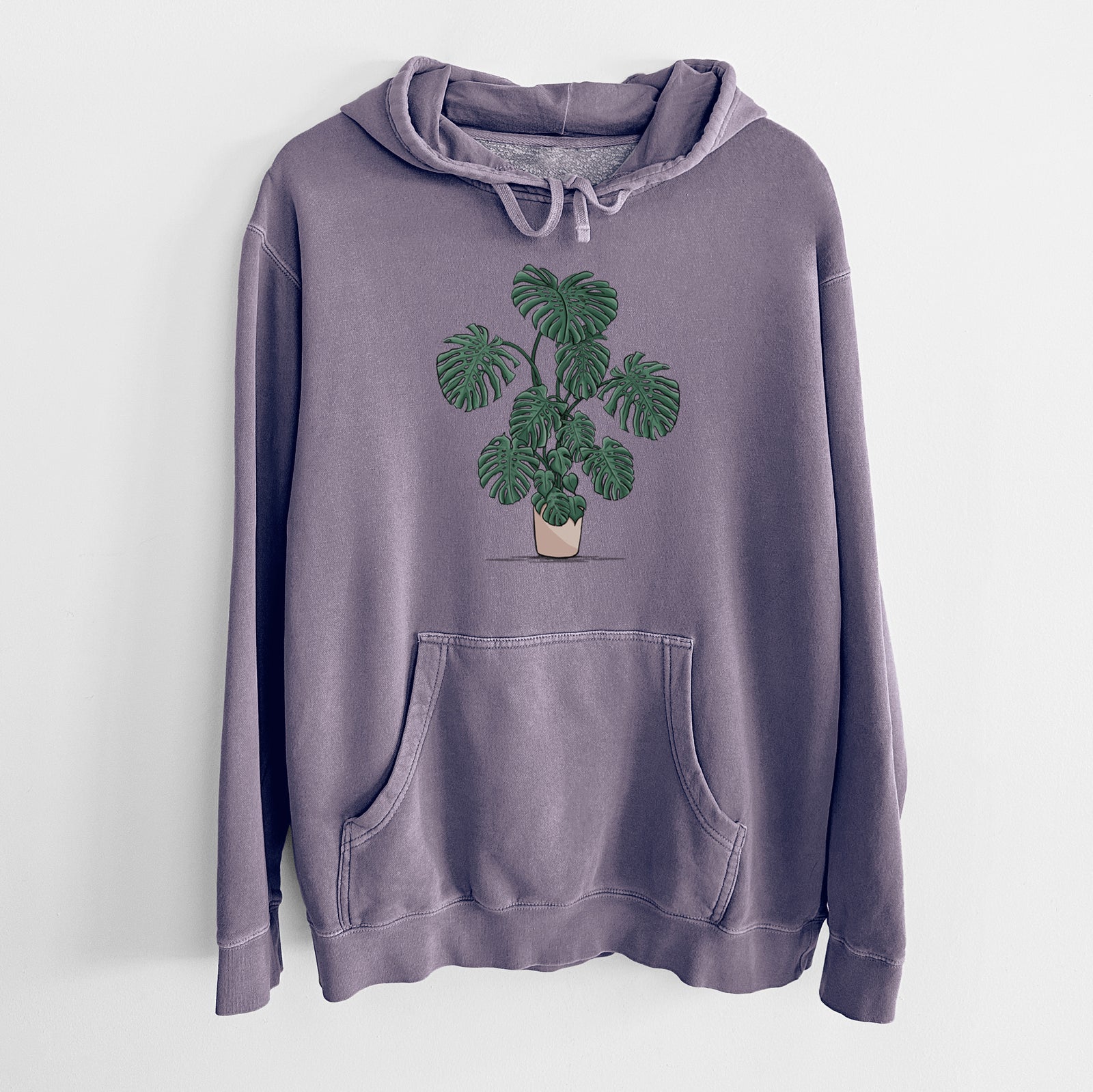 Plum purple pigment dyed hoodie laid flat, printed with a full-color illustration of a large potted Monstera plant.