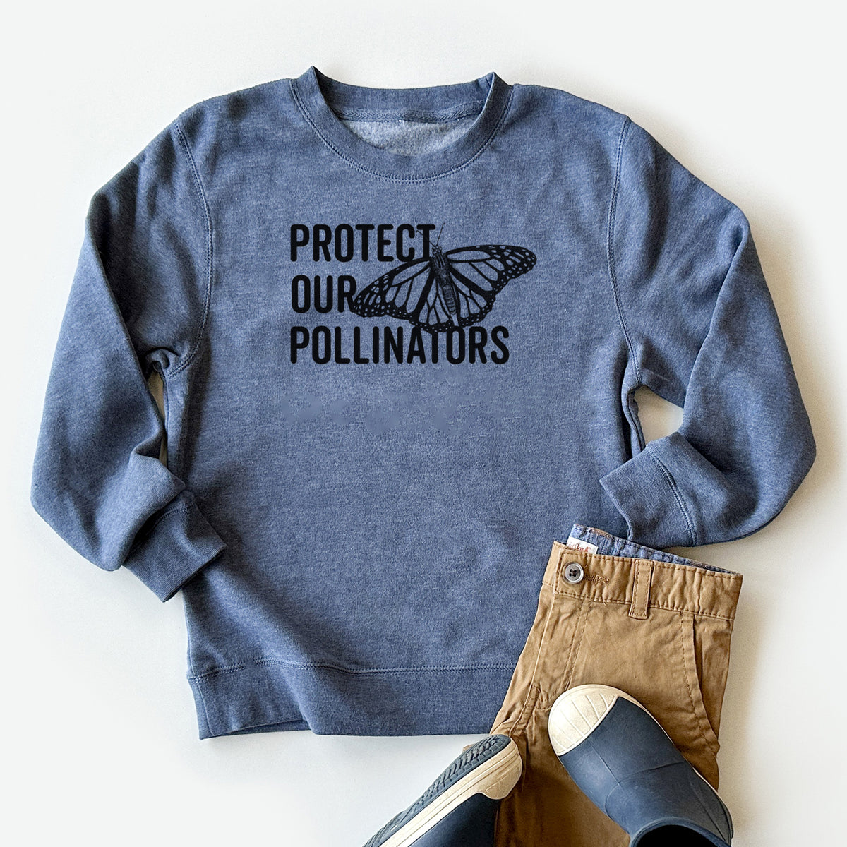 Youth crewneck sweatshirt printed with bold black words reading Protect Our Pollinators beside a monarch butterfly, styled flat with khaki pants and shoes.