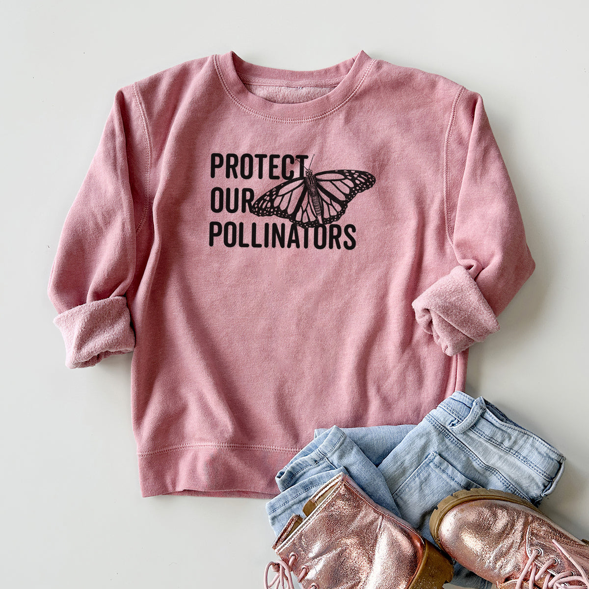 Youth crewneck sweatshirt printed with bold black words reading Protect Our Pollinators beside a monarch butterfly, styled flat with jeans and boots.
