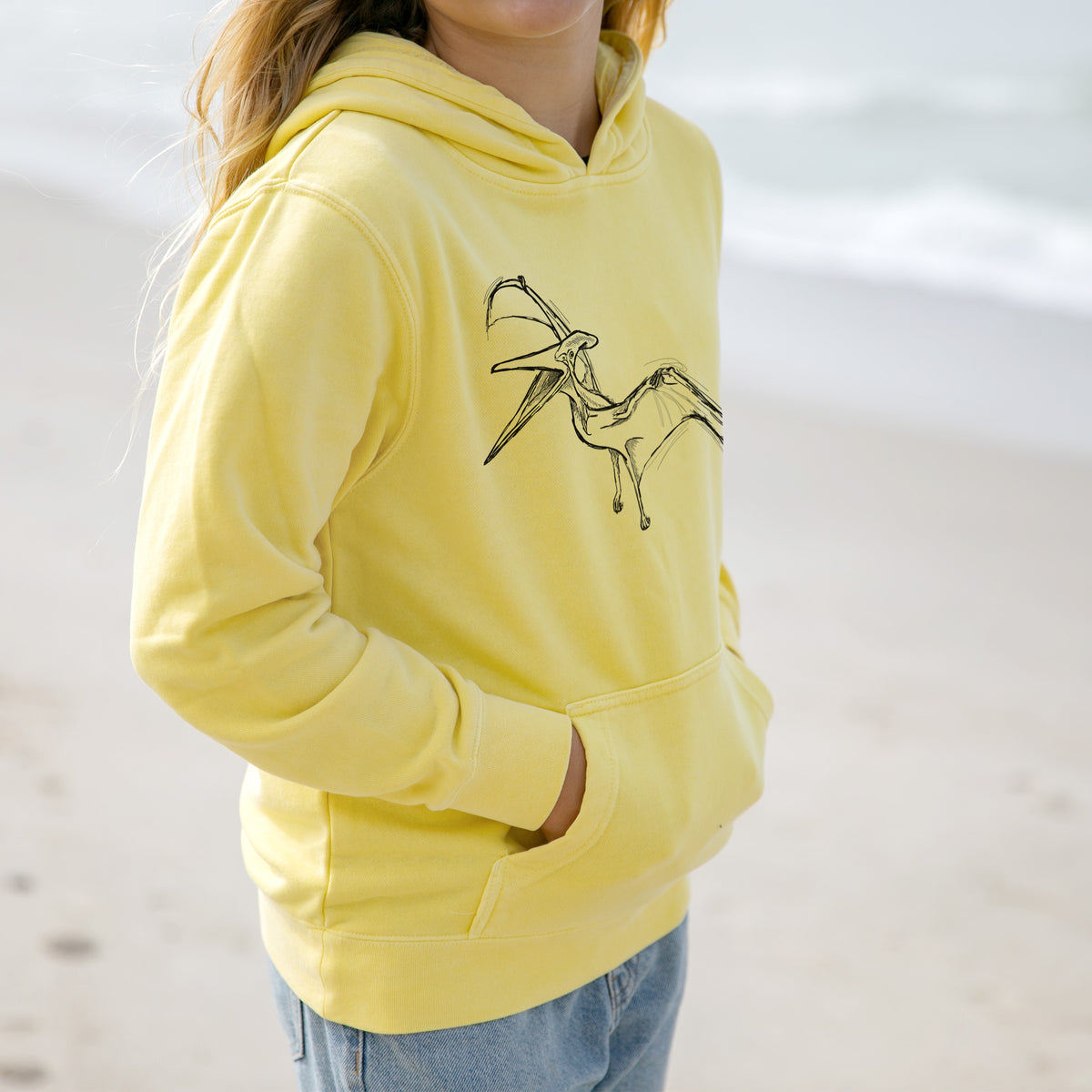 Girl wearing a youth pigment dyed hoodie printed with a black ink illustration of a Pteranodon in flight.
