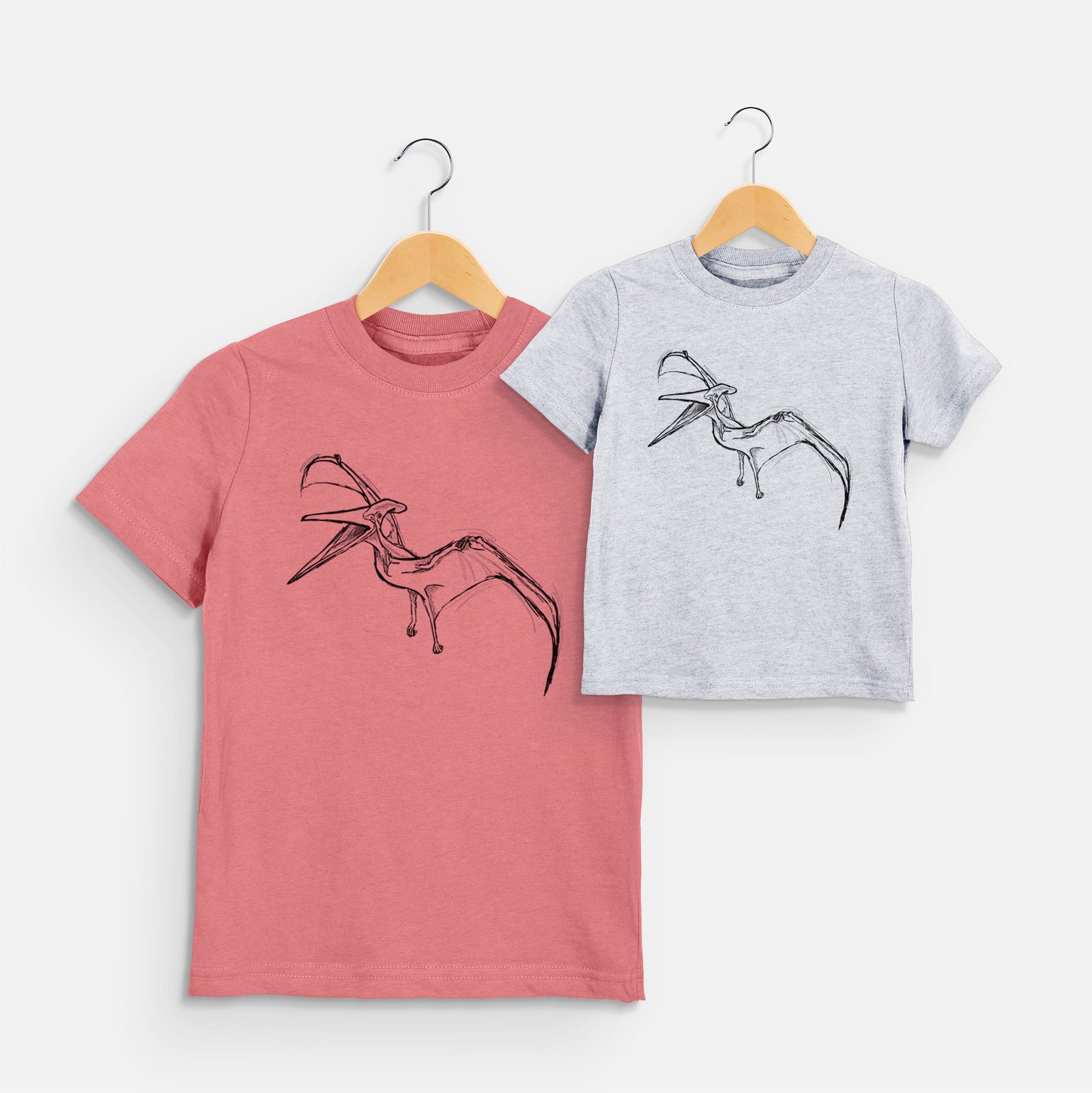 Two youth t-shirts in different colors on hangers, printed with a black ink illustration of a Pteranodon in flight.