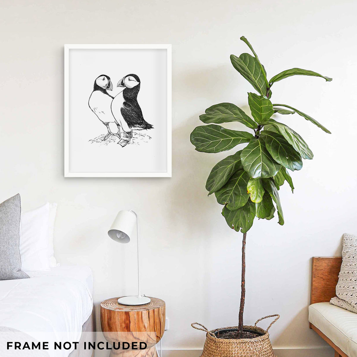 Art print of a detailed black ink illustration of two Atlantic puffins standing side by side, shown framed on a living room wall beside a potted plant. Frame not included.