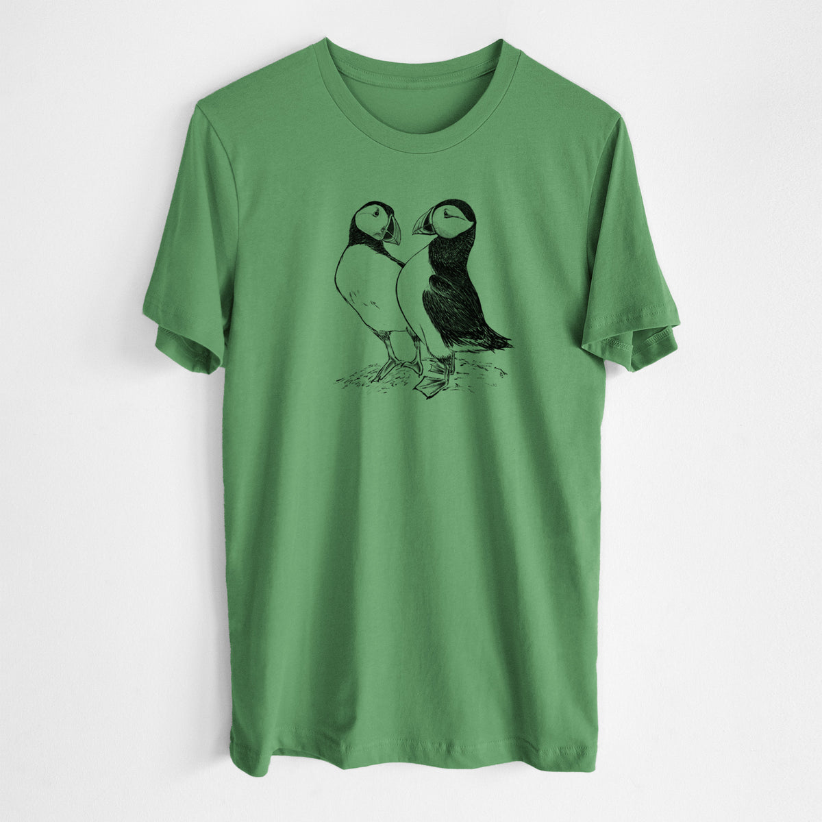 Leaf green lightweight cotton t-shirt laid flat, printed with a detailed black ink illustration of two Atlantic puffins standing side by side.
