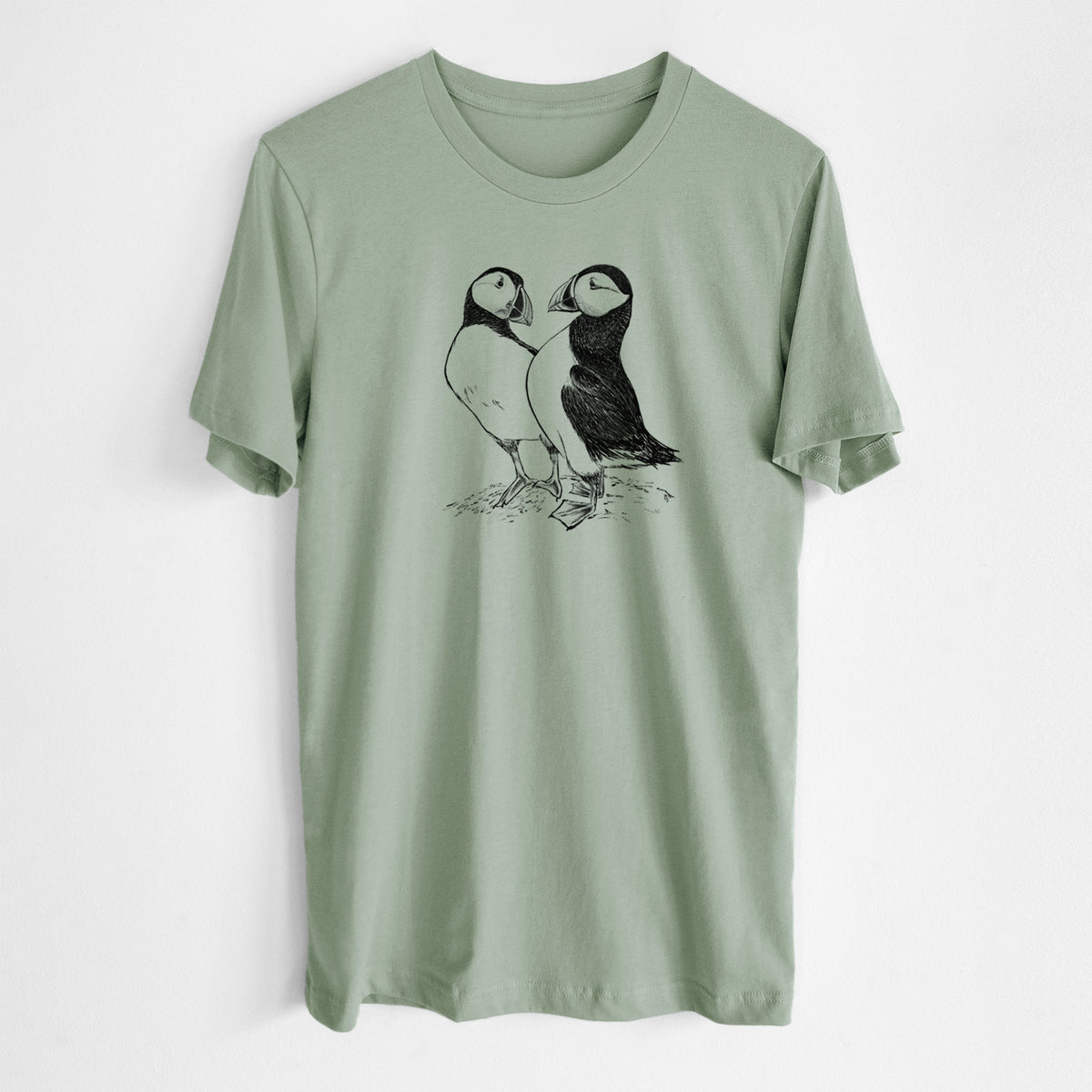Sage green lightweight cotton t-shirt laid flat, printed with a detailed black ink illustration of two Atlantic puffins standing side by side.