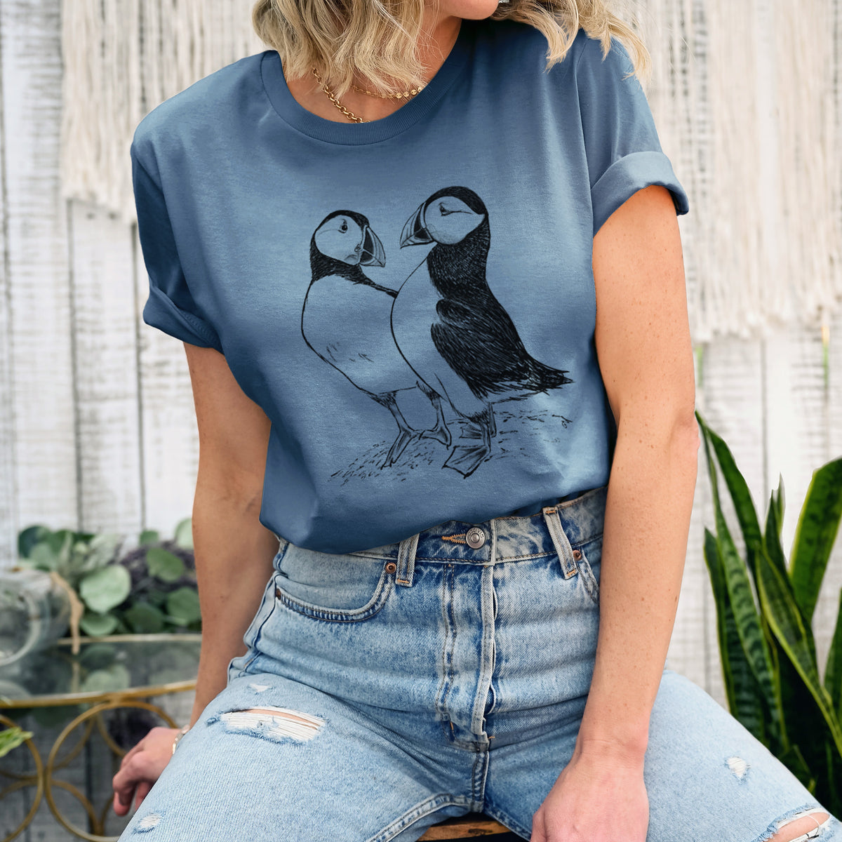 Woman wearing a steel blue lightweight cotton t-shirt printed with a detailed black ink illustration of two Atlantic puffins standing side by side.