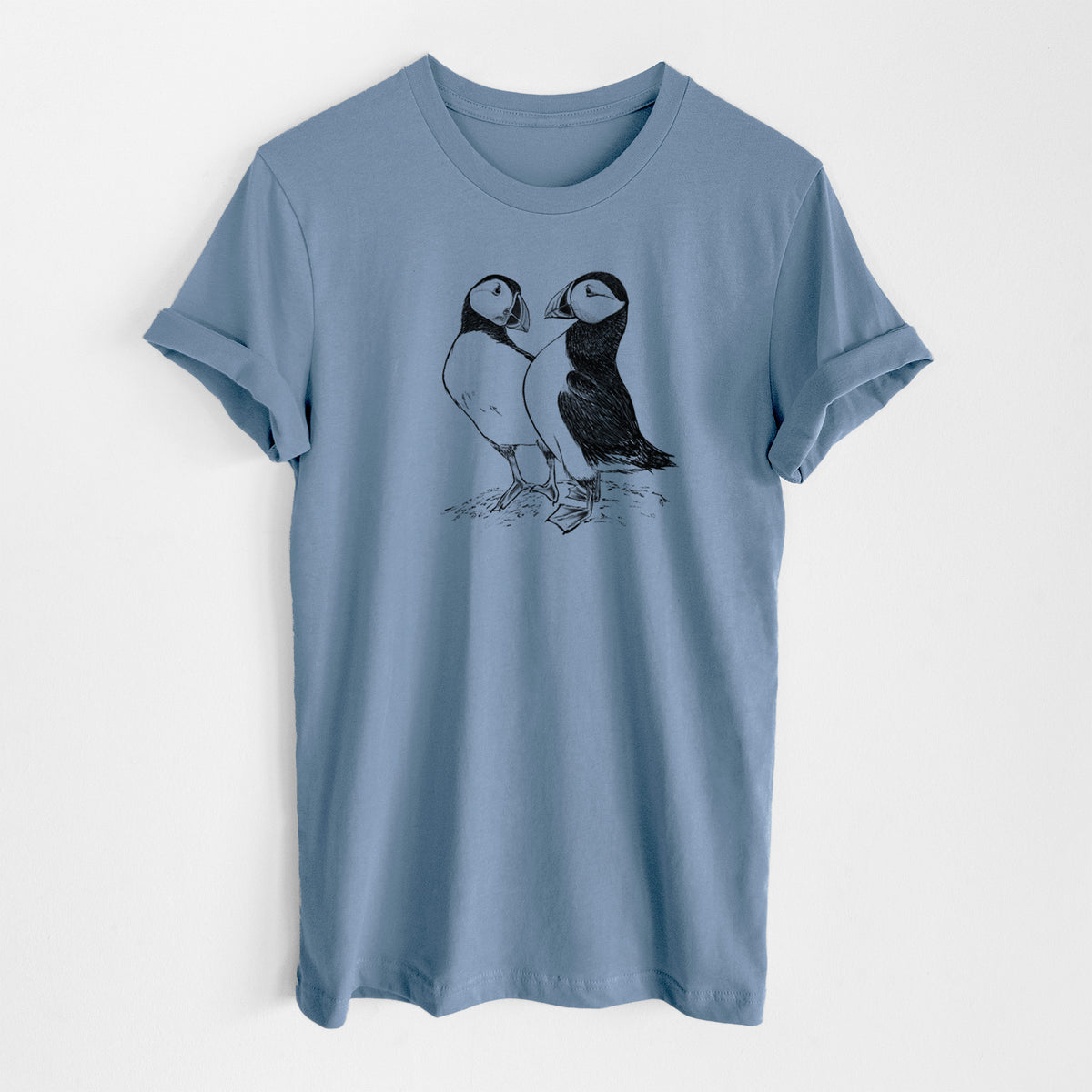 Steel blue lightweight cotton t-shirt laid flat, printed with a detailed black ink illustration of two Atlantic puffins standing side by side.