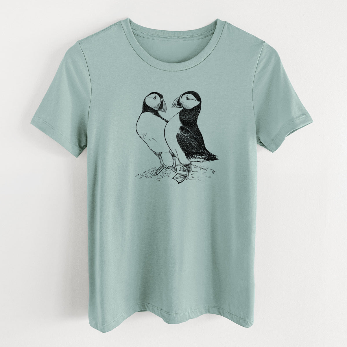 Dusty blue women's relaxed fit cotton t-shirt laid flat, printed with a detailed black ink illustration of two Atlantic puffins standing side by side.