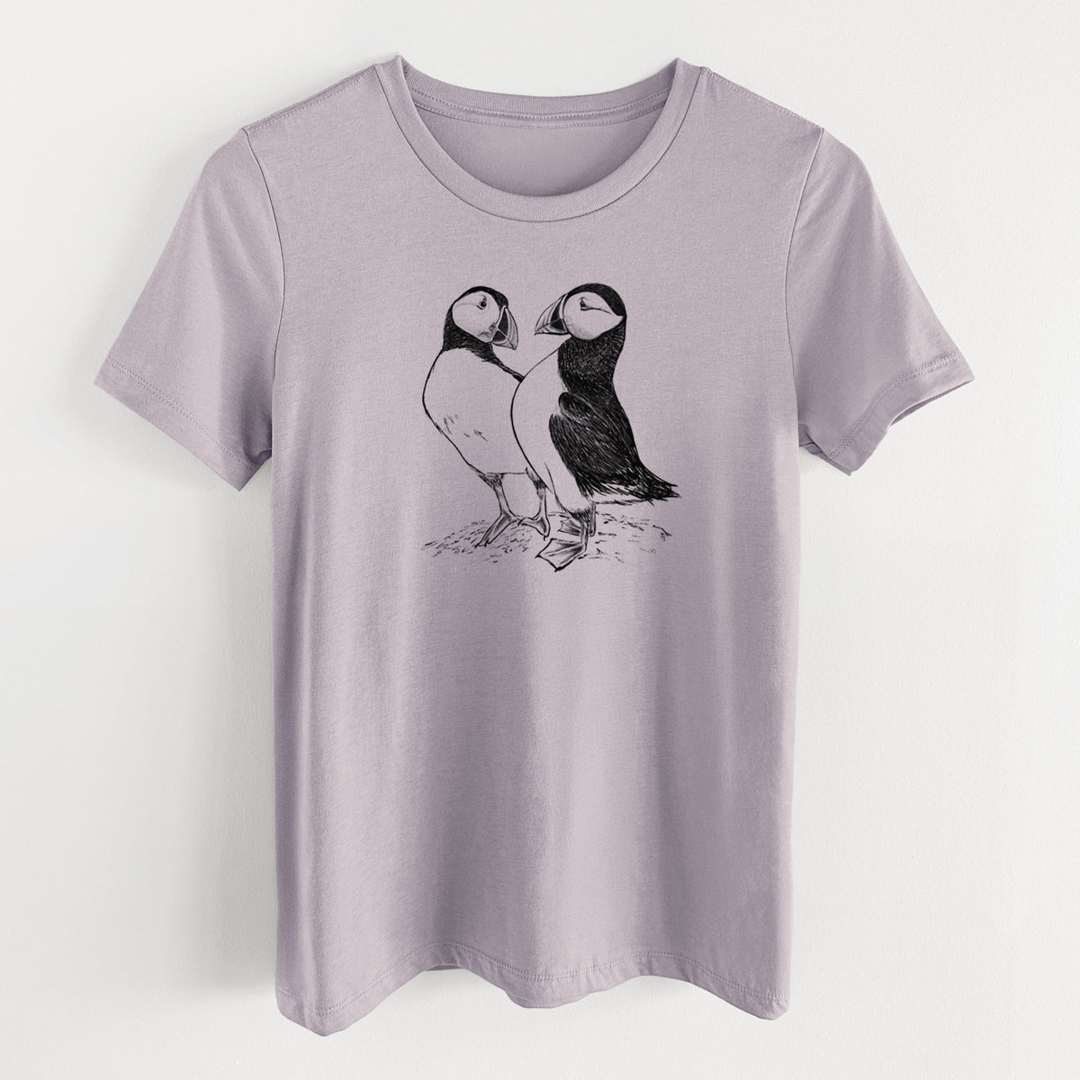 Light violet women's relaxed fit cotton t-shirt laid flat, printed with a detailed black ink illustration of two Atlantic puffins standing side by side.