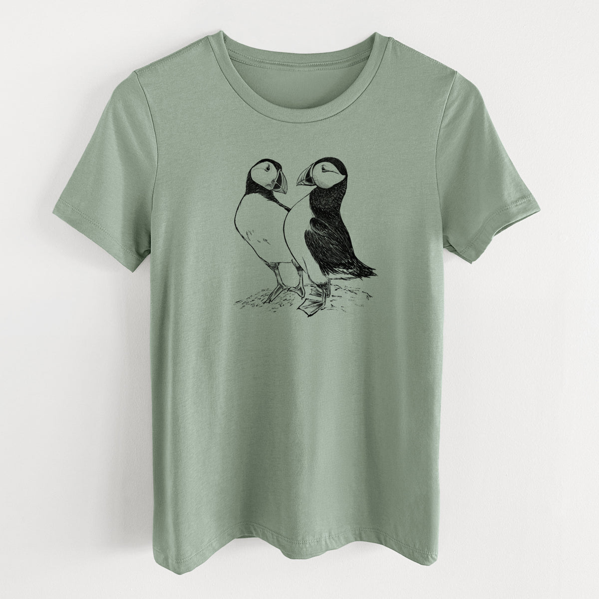 Sage green women's relaxed fit cotton t-shirt laid flat, printed with a detailed black ink illustration of two Atlantic puffins standing side by side.