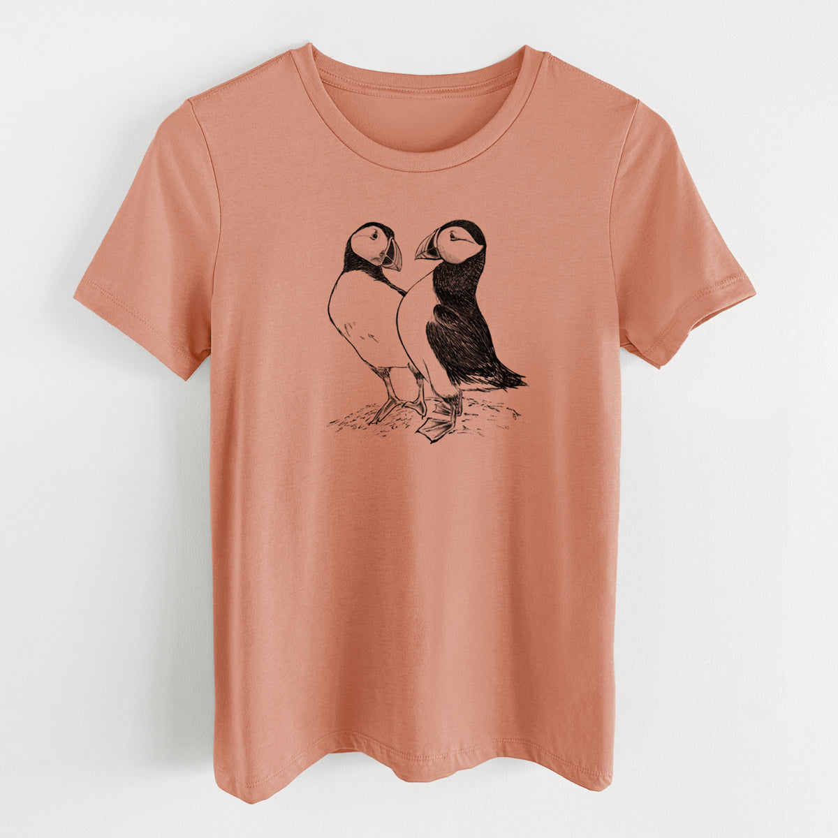 Terracotta orange women's relaxed fit cotton t-shirt laid flat, printed with a detailed black ink illustration of two Atlantic puffins standing side by side.