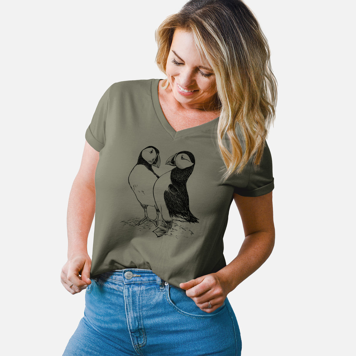 Woman wearing a military green women's relaxed fit cotton V-neck t-shirt printed with a detailed black ink illustration of two Atlantic puffins standing side by side.