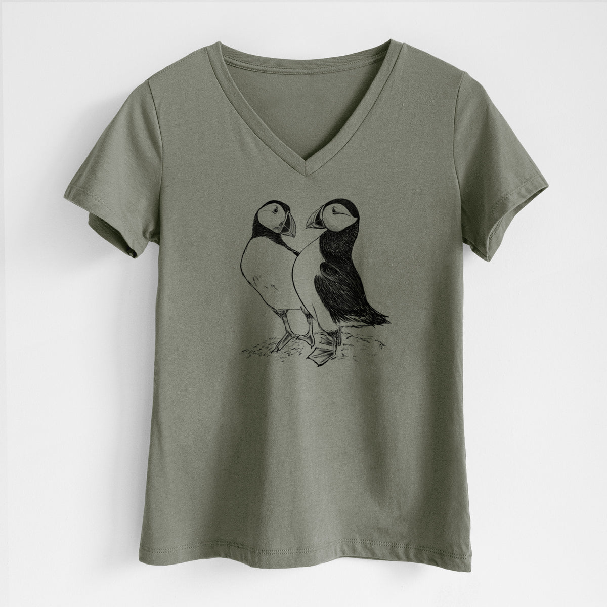 Military green women's relaxed fit cotton V-neck t-shirt laid flat, printed with a detailed black ink illustration of two Atlantic puffins standing side by side.