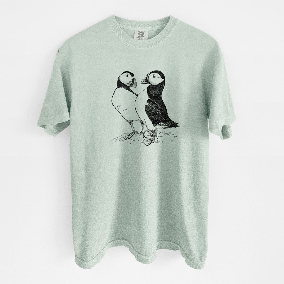 Bay green Comfort Colors t-shirt laid flat, printed with a detailed black ink illustration of two Atlantic puffins standing side by side.