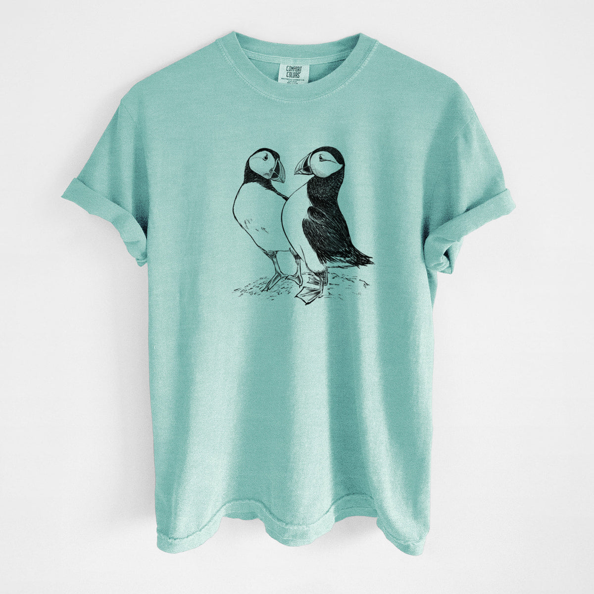 Chalky mint Comfort Colors t-shirt laid flat, printed with a detailed black ink illustration of two Atlantic puffins standing side by side.
