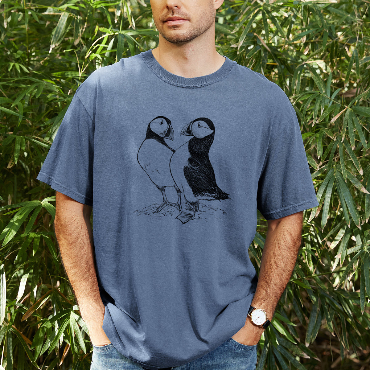 Man wearing a Comfort Colors t-shirt printed with a detailed black ink illustration of two Atlantic puffins standing side by side, outdoors.