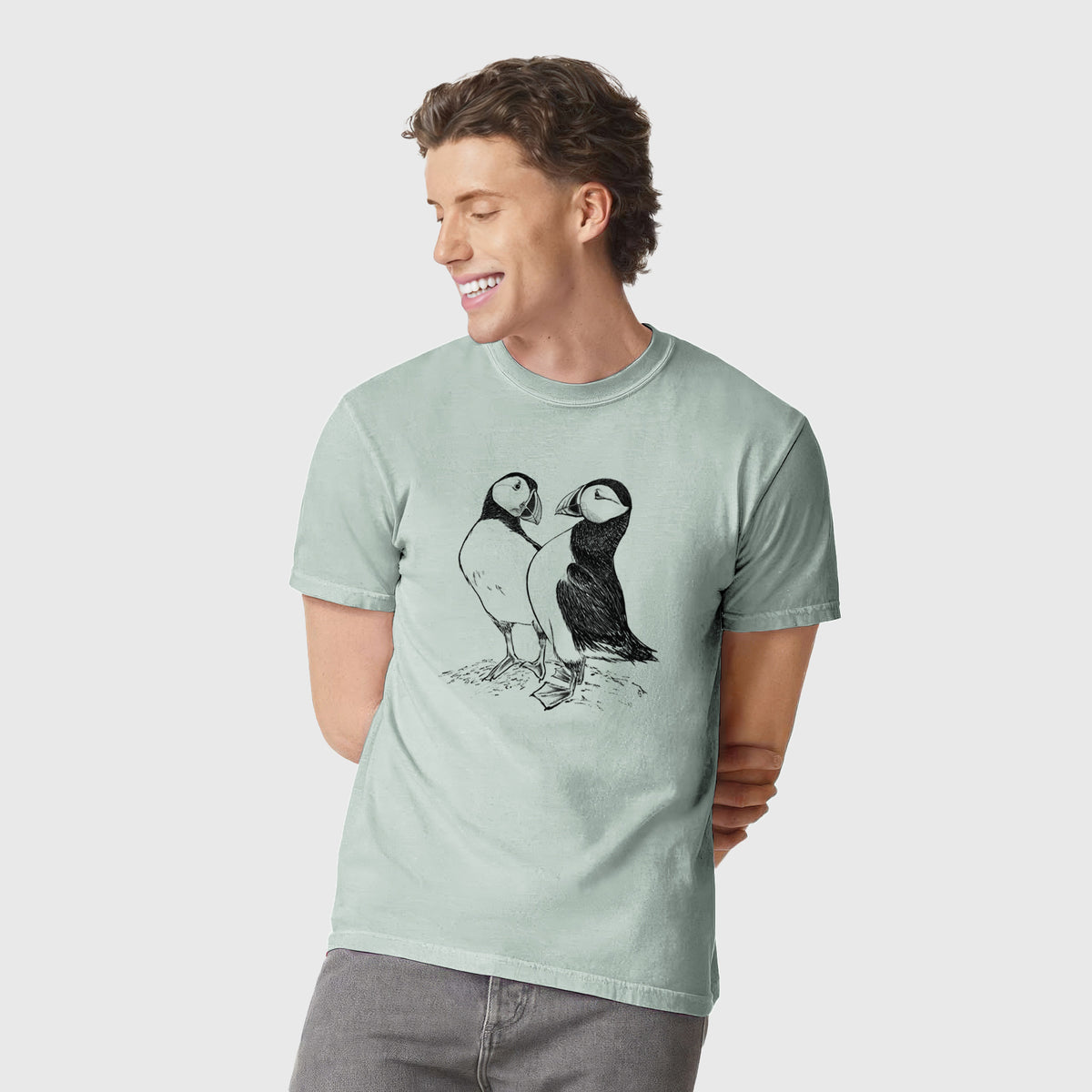 Man wearing a Comfort Colors t-shirt printed with a detailed black ink illustration of two Atlantic puffins standing side by side.