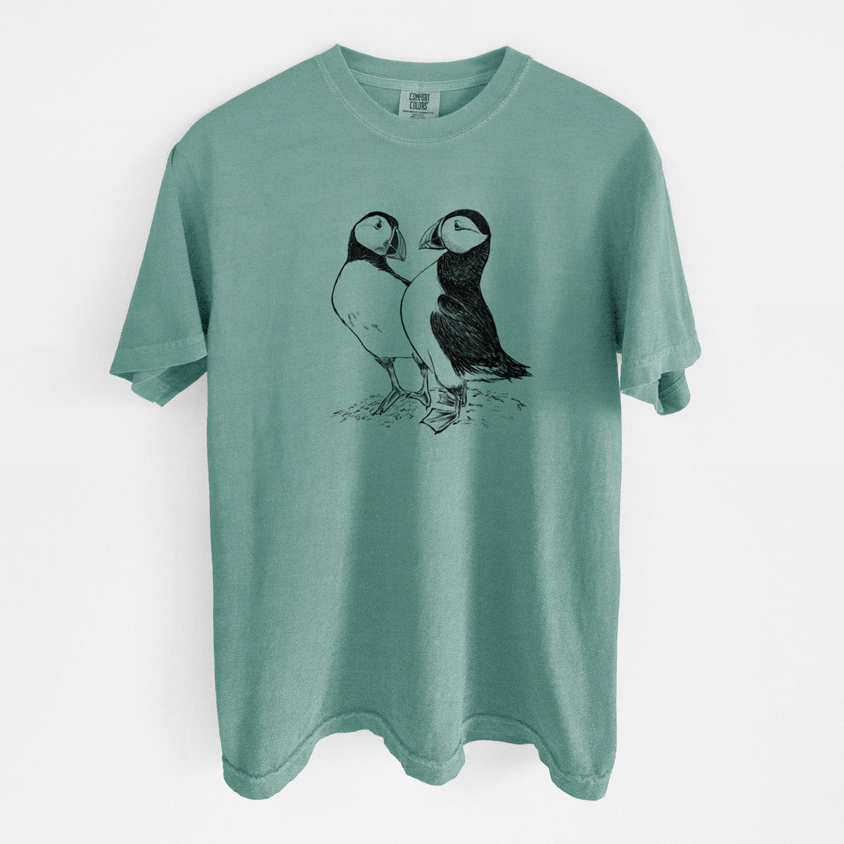 Reef green Comfort Colors t-shirt laid flat, printed with a detailed black ink illustration of two Atlantic puffins standing side by side.