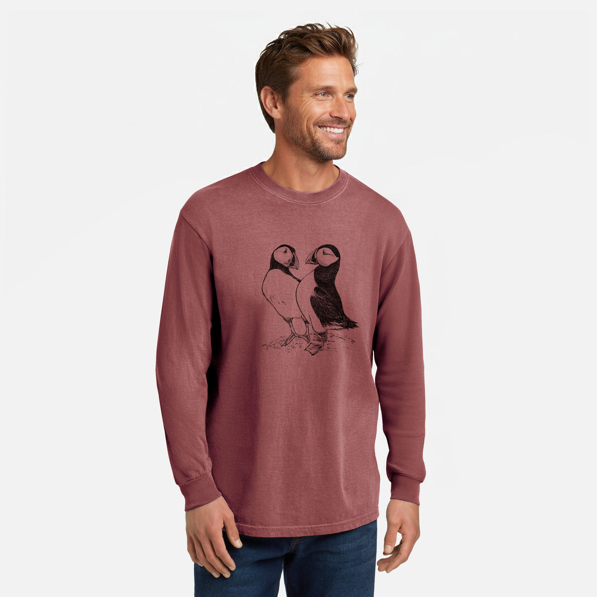 Brick red Comfort Colors long sleeve shirt printed with a detailed black ink illustration of two Atlantic puffins standing side by side, shown in a lifestyle photo.