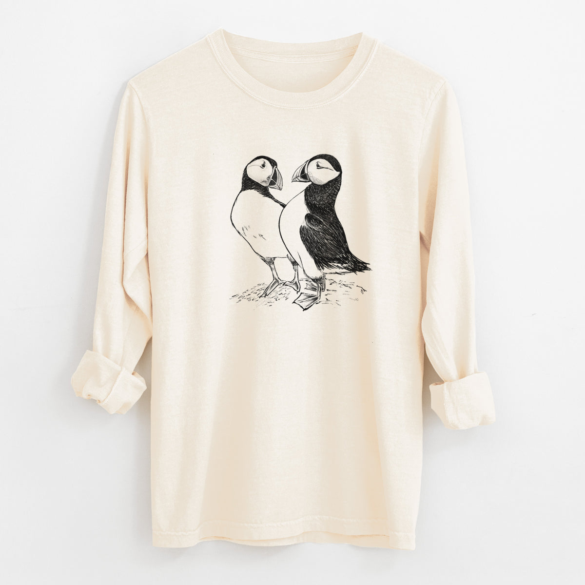 Ivory Comfort Colors long sleeve shirt laid flat with the cuffs rolled, printed with a detailed black ink illustration of two Atlantic puffins standing side by side.