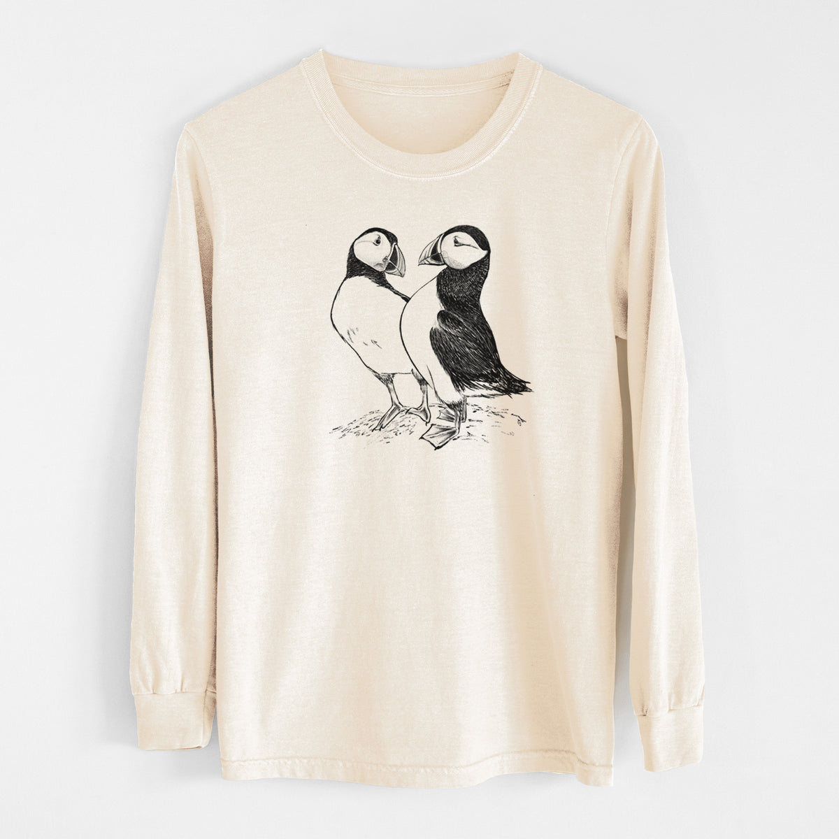 Ivory Comfort Colors long sleeve shirt laid flat, printed with a detailed black ink illustration of two Atlantic puffins standing side by side.