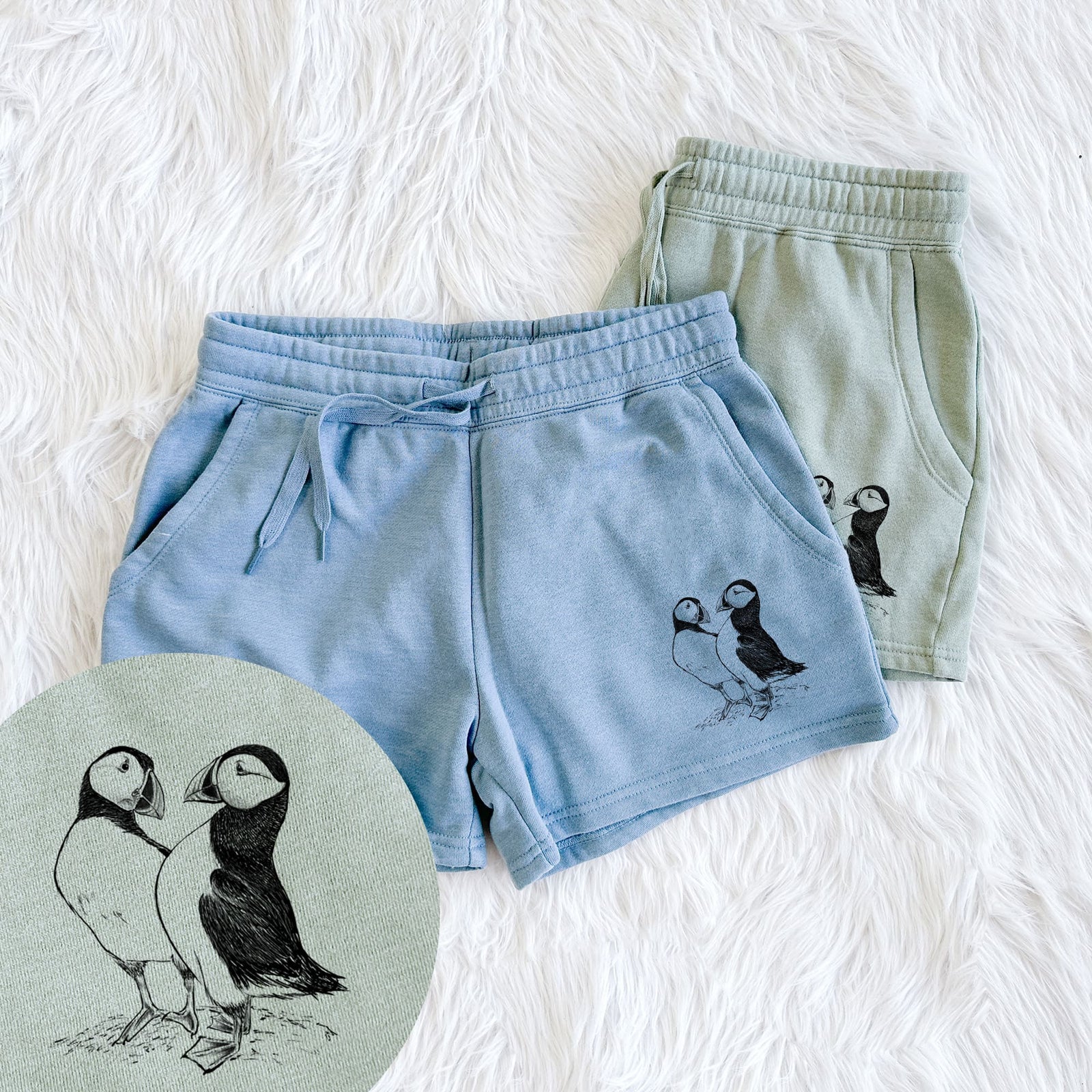 Two pairs of Cali Wave shorts in different colors printed with a detailed black ink illustration of two Atlantic puffins standing side by side, with a close-up of the print.