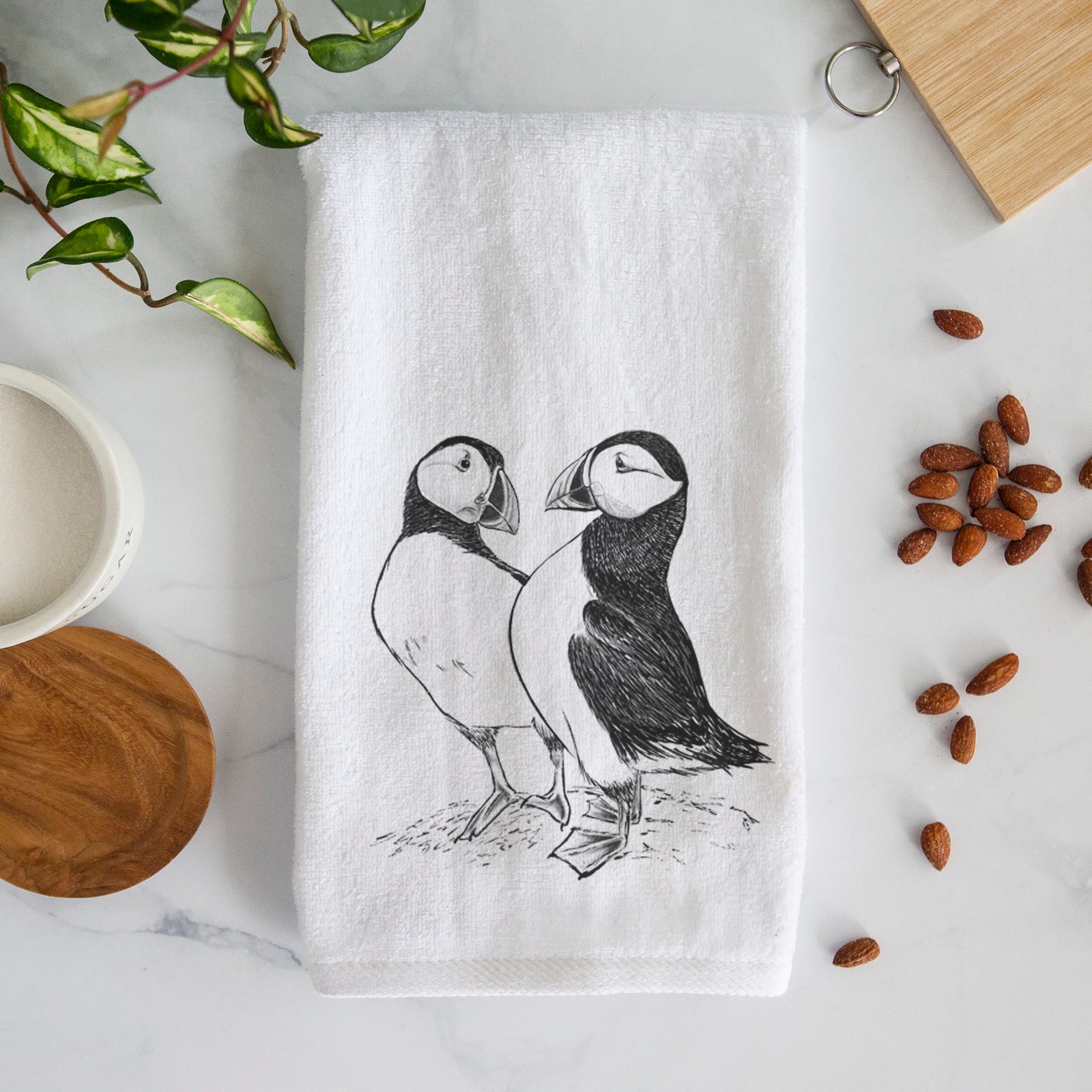 White hand towel printed with a detailed black ink illustration of two Atlantic puffins standing side by side.
