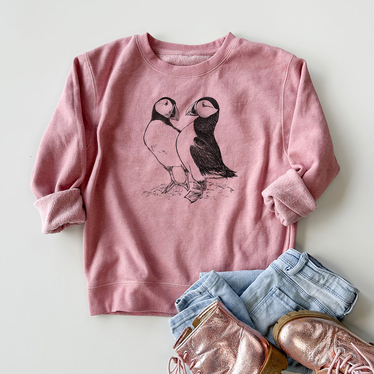 Youth crewneck sweatshirt printed with a detailed black ink illustration of two Atlantic puffins standing side by side, styled flat with jeans and boots.