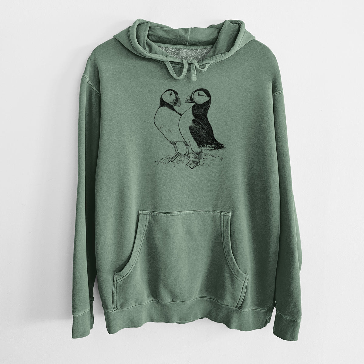 Alpine green pigment dyed hoodie laid flat, printed with a detailed black ink illustration of two Atlantic puffins standing side by side.
