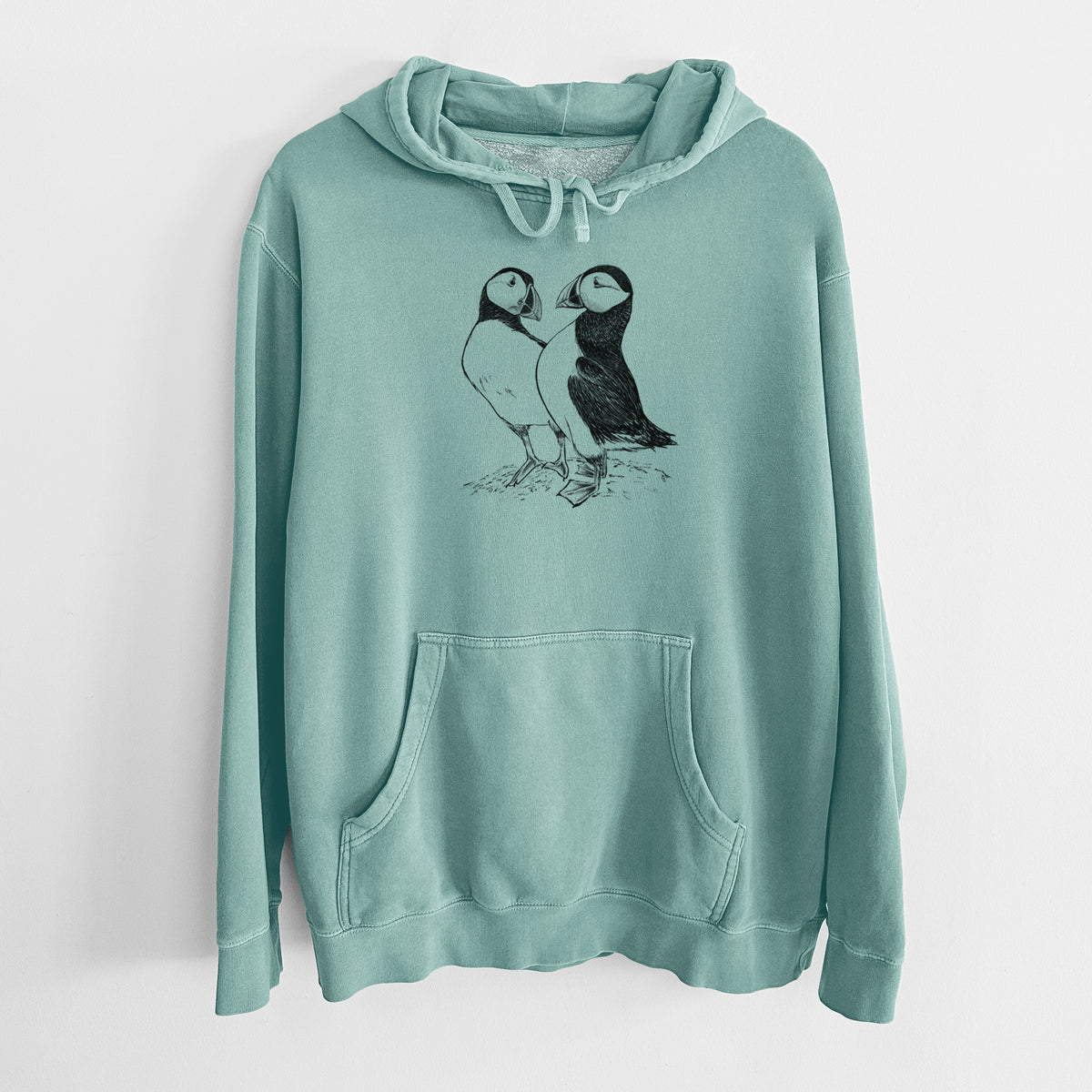 Mint green pigment dyed hoodie laid flat, printed with a detailed black ink illustration of two Atlantic puffins standing side by side.