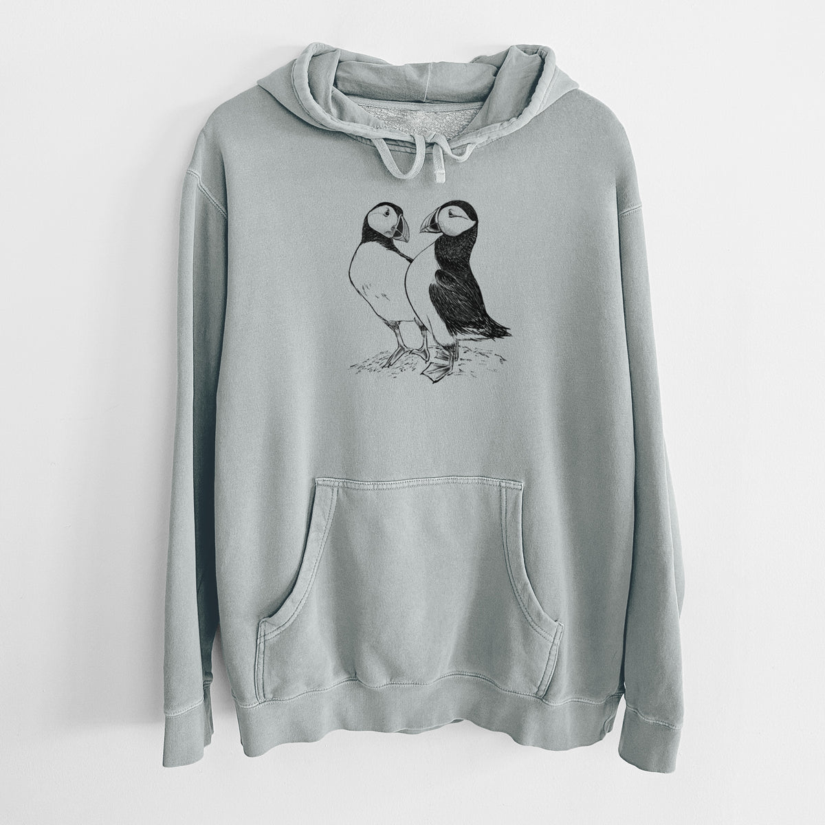 Sage green pigment dyed hoodie laid flat, printed with a detailed black ink illustration of two Atlantic puffins standing side by side.
