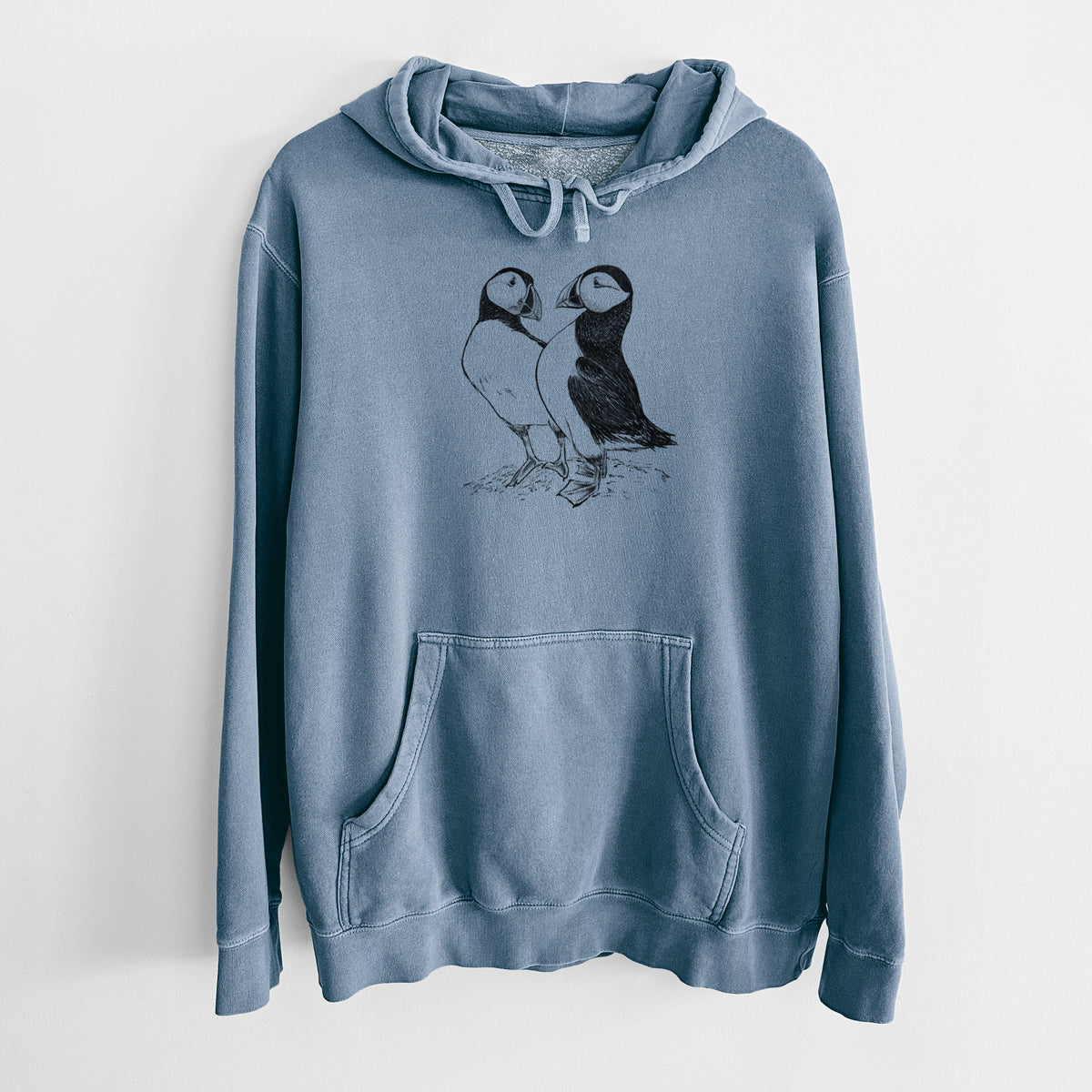 Slate blue pigment dyed hoodie laid flat, printed with a detailed black ink illustration of two Atlantic puffins standing side by side.