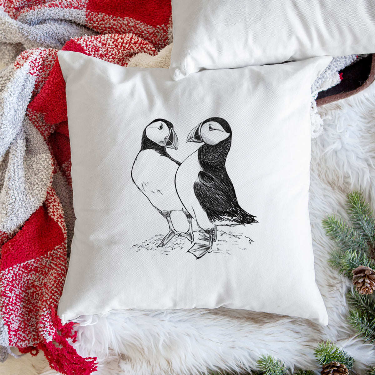 White pillow cover printed with a detailed black ink illustration of two Atlantic puffins standing side by side, on a woven chair.