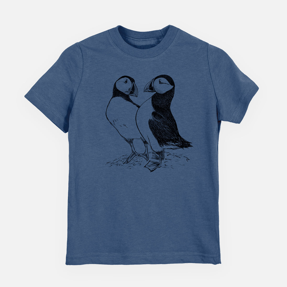 Indigo blue youth t-shirt laid flat, printed with a detailed black ink illustration of two Atlantic puffins standing side by side.