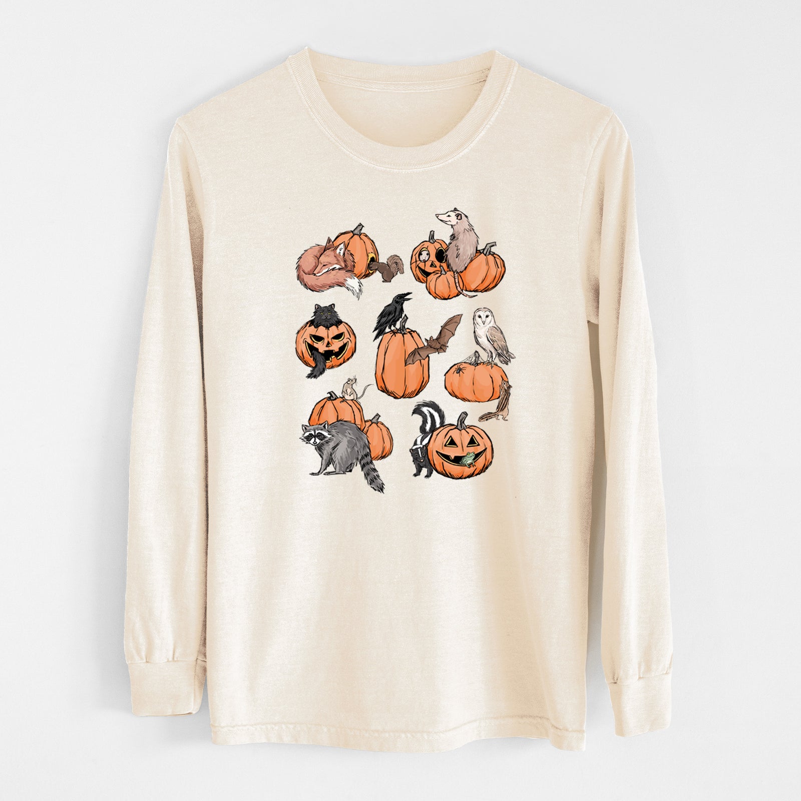 Ivory Comfort Colors long sleeve shirt laid flat, printed with orange carved jack-o'-lanterns with black ink opossums, raccoons, owls and skunks peeking out.