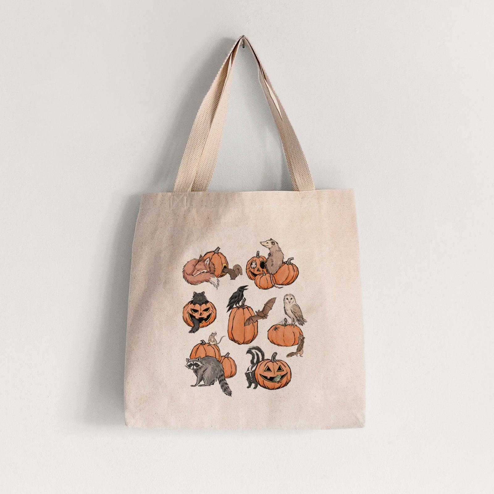 Natural canvas tote bag printed with orange carved jack-o'-lanterns with black ink opossums, raccoons, owls and skunks peeking out.