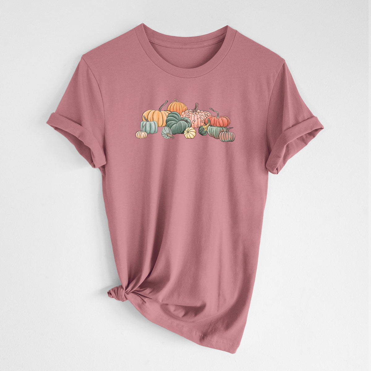 Mauve pink lightweight cotton t-shirt laid flat with the sleeves rolled, printed with a full-color illustration of a pile of pumpkins and gourds in orange, green and white.