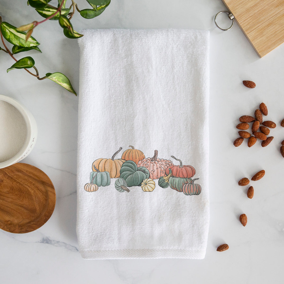 White hand towel printed with a full-color illustration of a pile of pumpkins and gourds in orange, green and white.