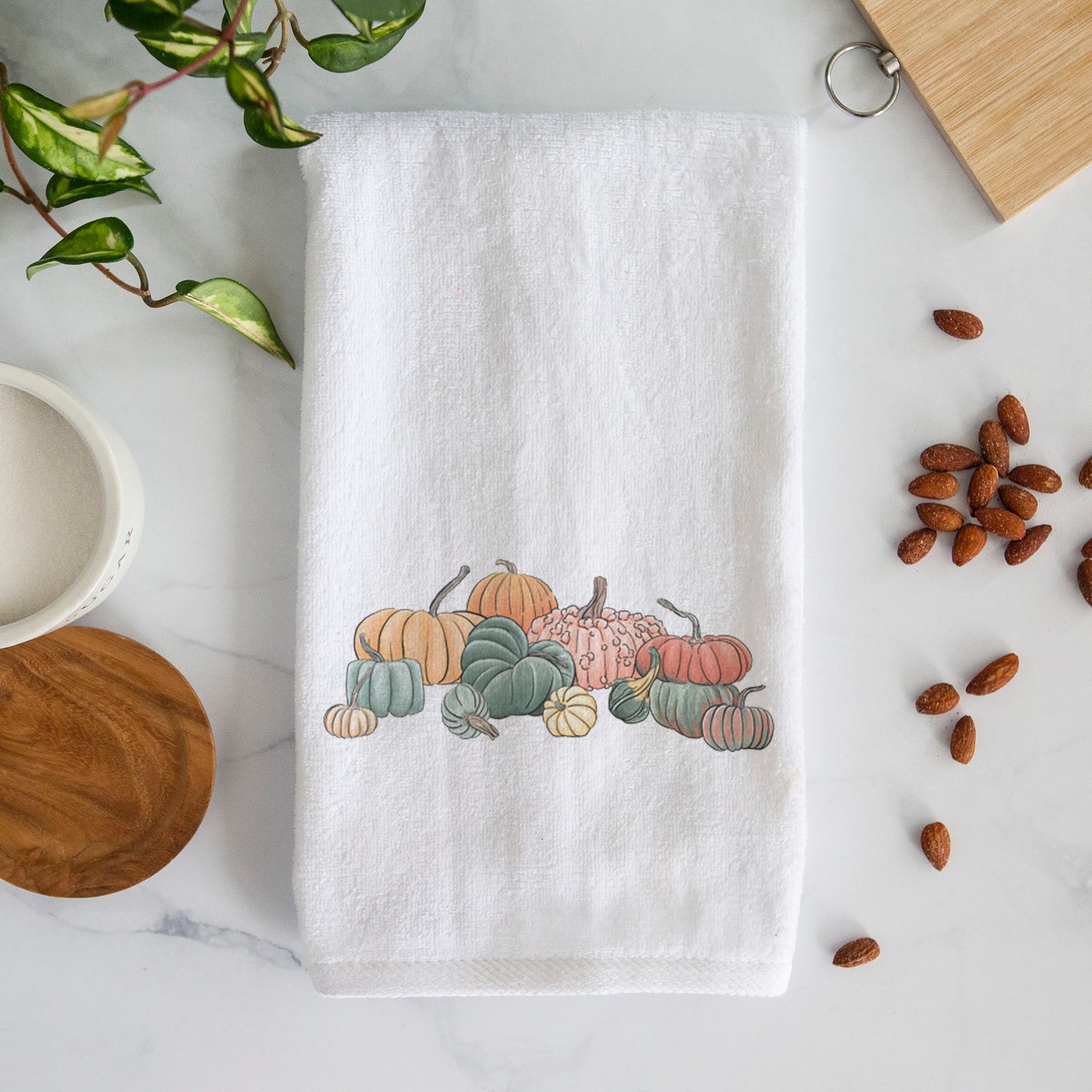 White hand towel printed with a full-color illustration of a pile of pumpkins and gourds in orange, green and white.