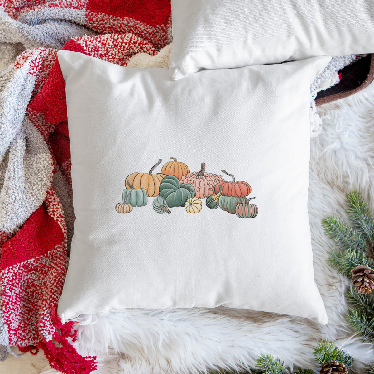 White pillow cover printed with a full-color illustration of a pile of pumpkins and gourds in orange, green and white, on a woven chair.