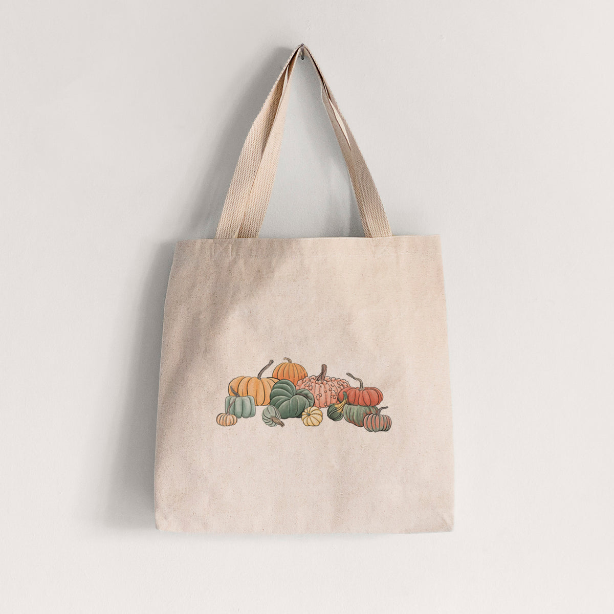 Natural canvas tote bag printed with a full-color illustration of a pile of pumpkins and gourds in orange, green and white.