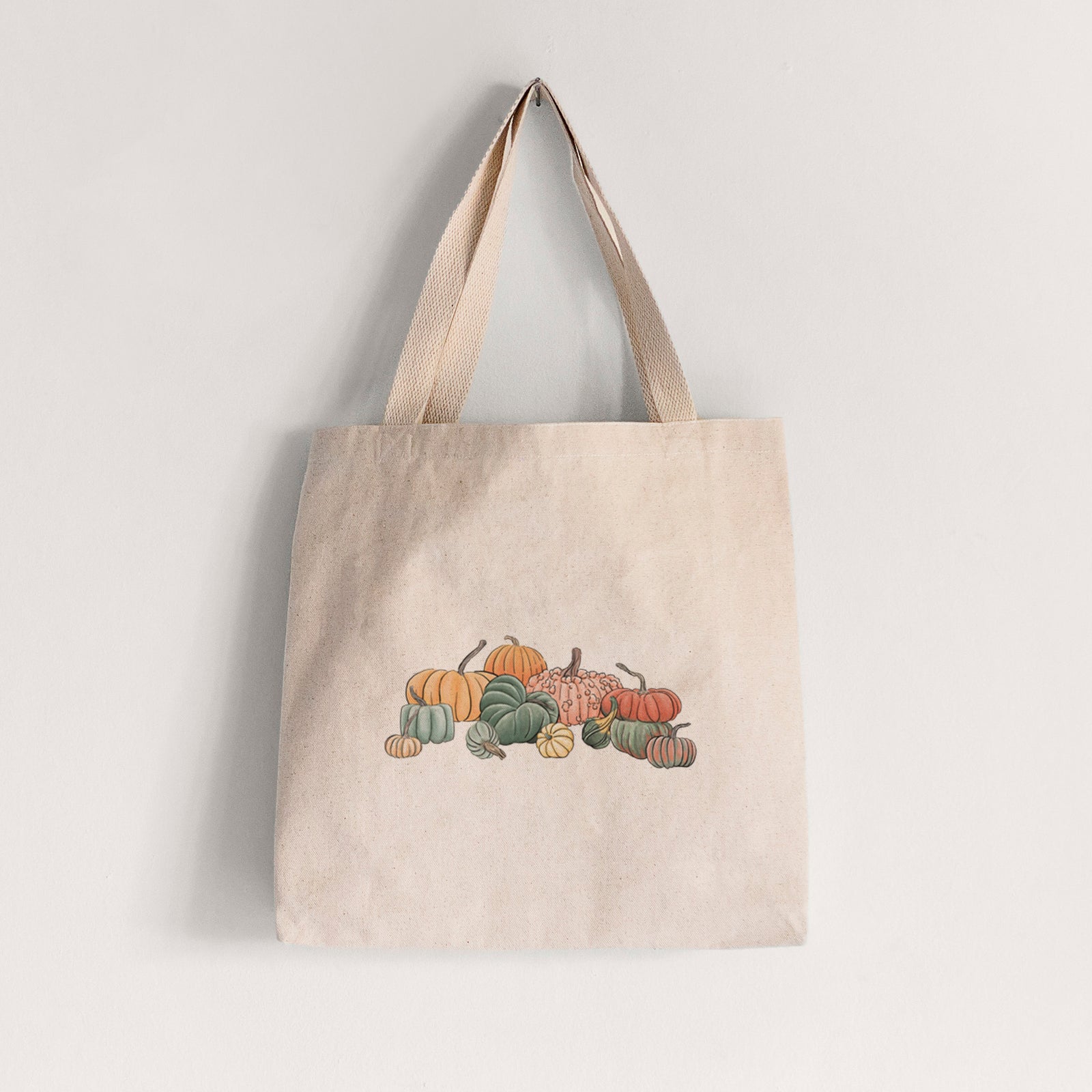 Natural canvas tote bag printed with a full-color illustration of a pile of pumpkins and gourds in orange, green and white.