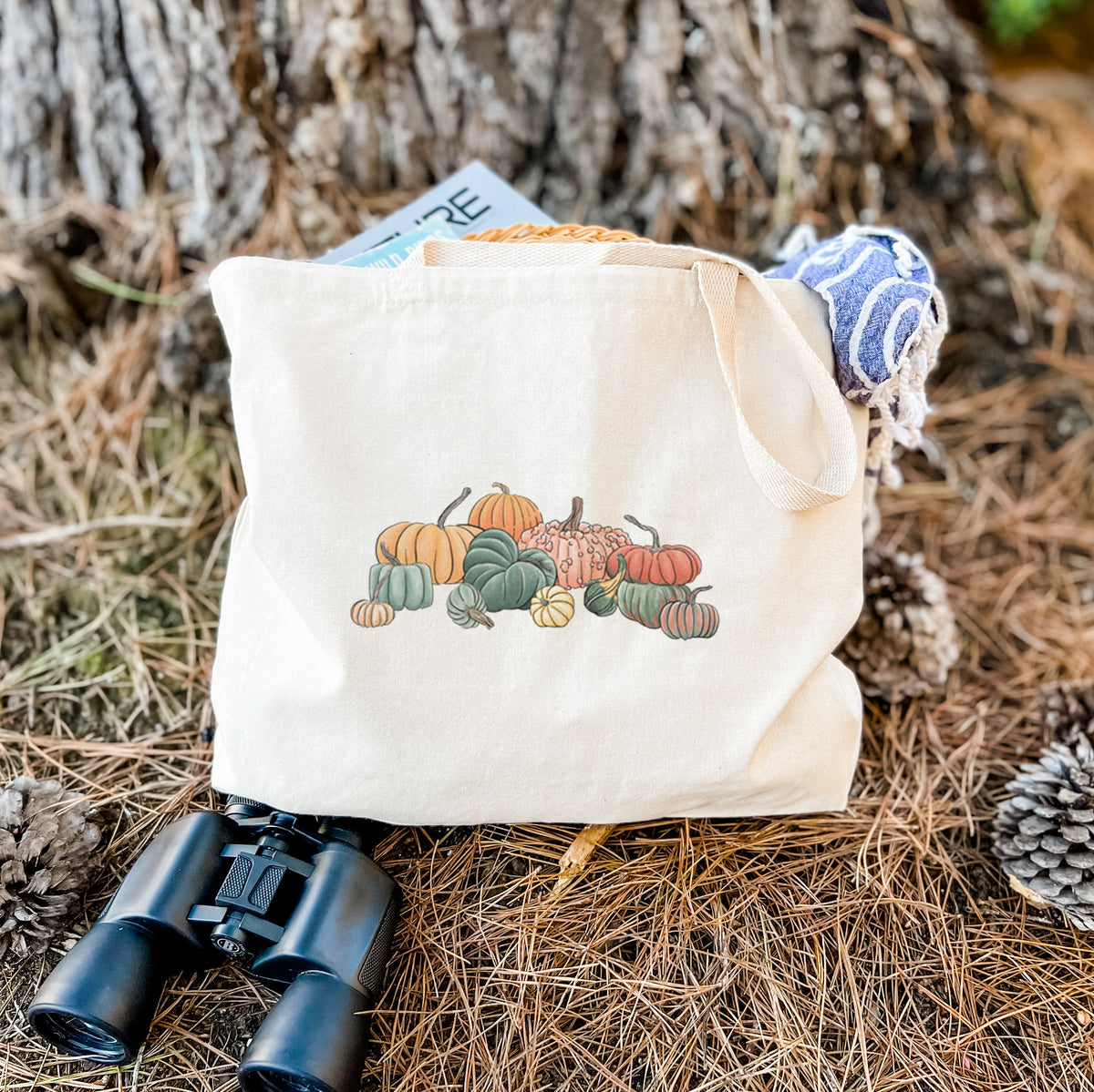 Canvas tote bag printed with a full-color illustration of a pile of pumpkins and gourds in orange, green and white, resting on dry grass beside a pair of binoculars.