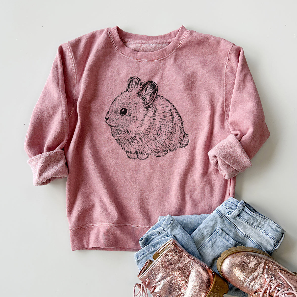 Youth crewneck sweatshirt printed with a detailed black ink illustration of a round, fluffy pygmy rabbit, styled flat with jeans and boots.