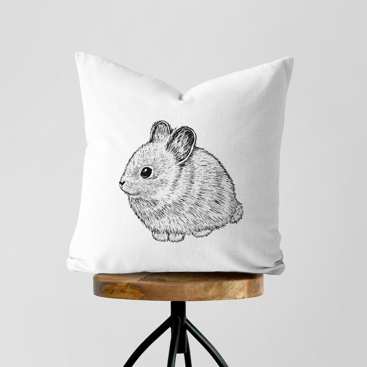 White pillow cover printed with a detailed black ink illustration of a round, fluffy pygmy rabbit, on a wooden stool.