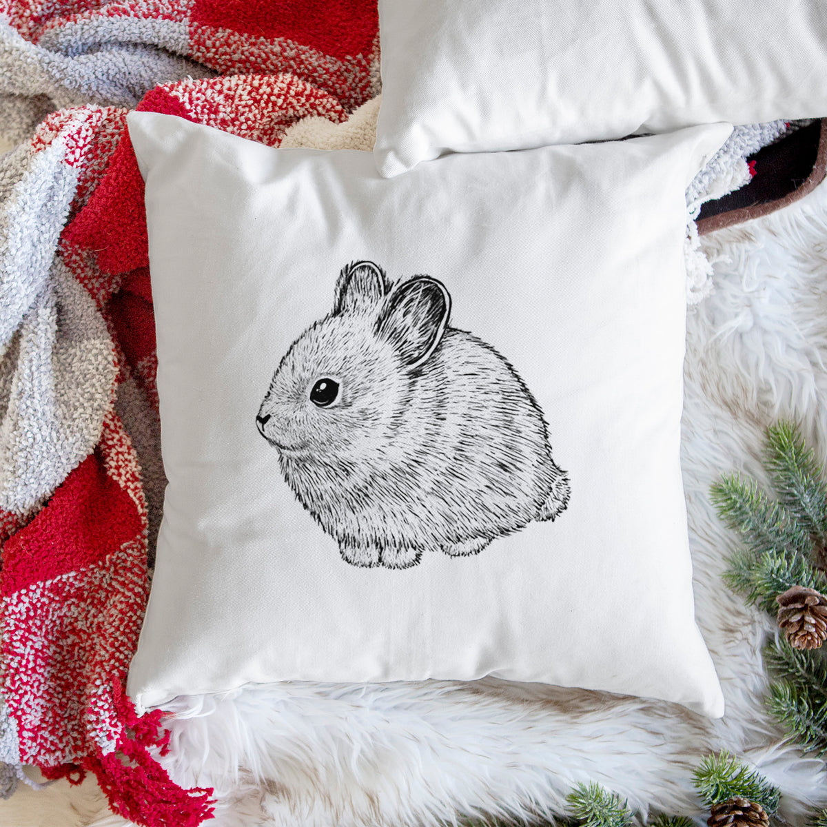 White pillow cover printed with a detailed black ink illustration of a round, fluffy pygmy rabbit, on a woven chair.
