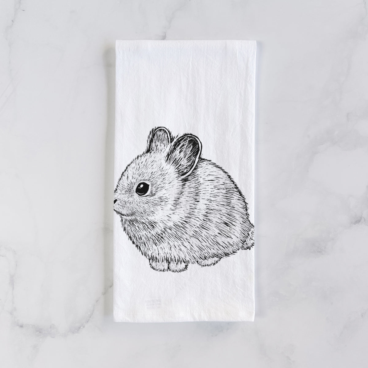 White cotton tea towel laid flat on marble, printed with a detailed black ink illustration of a round, fluffy pygmy rabbit.
